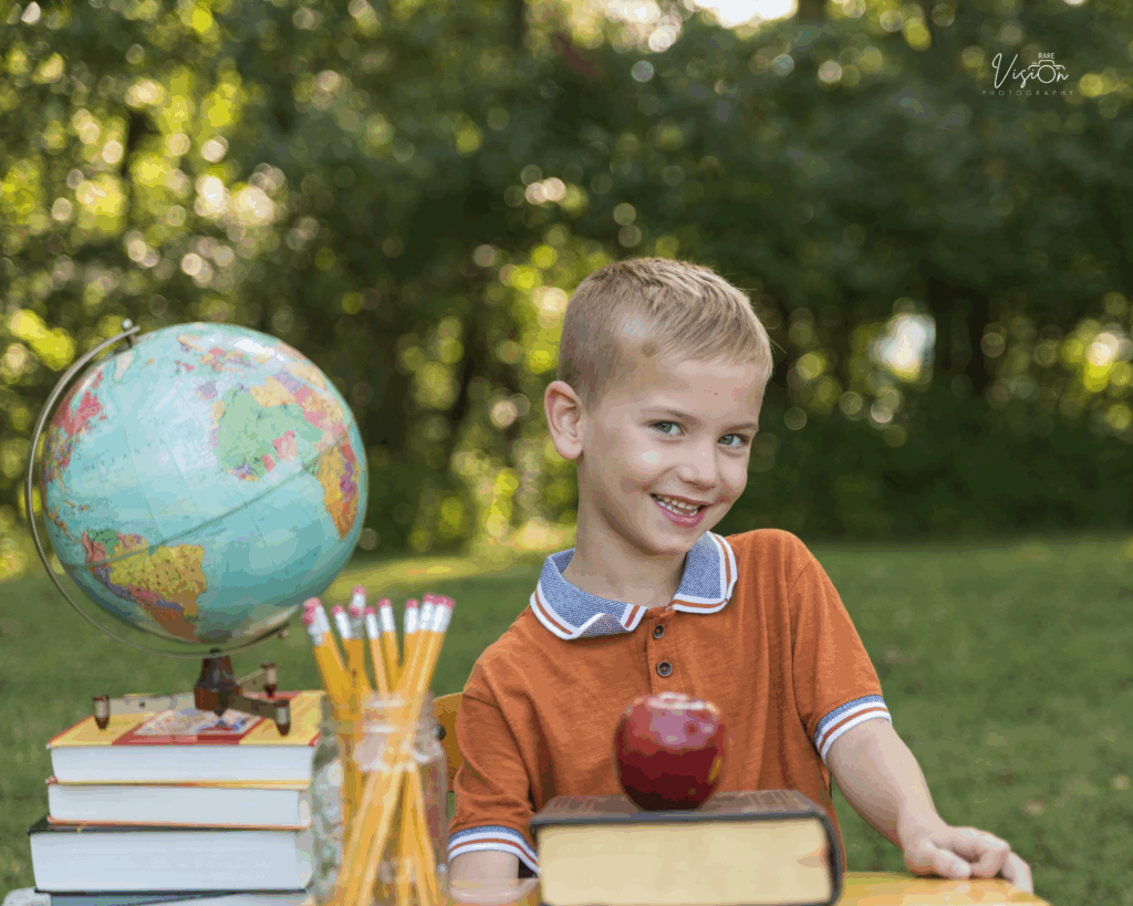 Image of boy at school desk with books, globe, apple, pencils