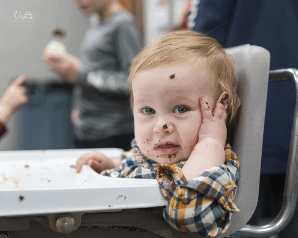 Image of birthday boy with cake on face sitting in high chair